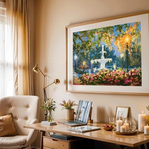 May include: A framed painting of a fountain in a park, with a wooden desk, laptop, and candles in front of it. The painting features a white fountain, pink flowers, and lush greenery. The room has beige walls and curtains, with a gold desk lamp and a beige armchair.