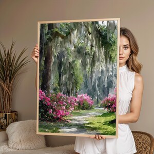 May include: A framed landscape painting depicts a path winding through a lush forest. Pink azaleas line the path, with Spanish moss hanging from the trees. The artwork is in a light wooden frame.