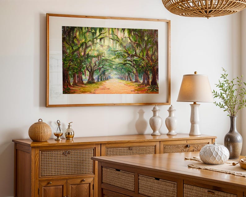 May include: A framed landscape painting of a tree-lined path with sunlight filtering through the branches. The artwork is in a wooden frame and hangs above a wooden cabinet with decorative items, including a lamp and vases. The scene evokes a sense of tranquility.