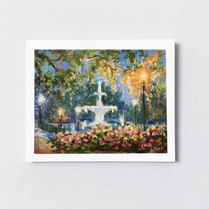 May include: An oil painting of a park scene at dusk. A white fountain is the focal point, surrounded by pink flowers and lush greenery. The painting captures the soft glow of streetlights and the evening sky.