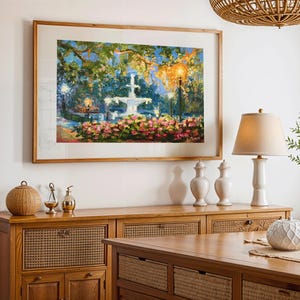 May include: A framed painting of a fountain in a garden, with pink and red flowers in the foreground. The painting is displayed above a wooden cabinet with decorative items, including a lamp and vases. A woven light fixture hangs from the ceiling.