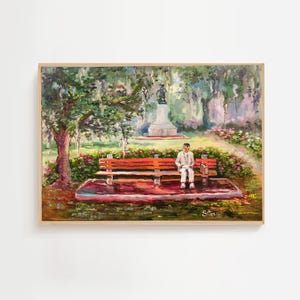 Op de afbeelding: Een ingelijst schilderij toont een parkscène met een rode bank en een persoon die erop zit. Het kunstwerk toont een standbeeld, bomen en bloemen, met een zachte, impressionistische stijl. Het schilderij is rechtsonder gesigneerd.