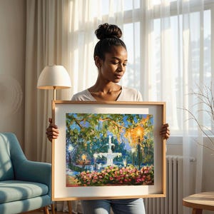 May include: A framed painting of a fountain in a park, with a wooden frame. The artwork features a white fountain, lush greenery, and colorful flowers. The painting is held by a person.