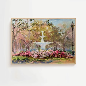Op de afbeelding: Olieverfschilderij van een parkscène met een fontein, bomen en bloemen. Het kunstwerk toont een witte fontein, omringd door roze en rode bloemen. Een zwarte lantaarnpaal staat rechts. Het schilderij is ingelijst in een lichte houten lijst.