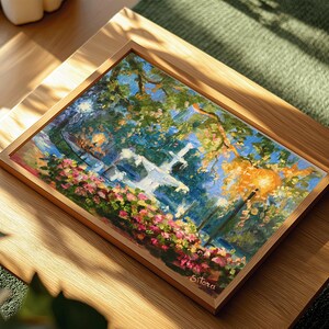 May include: A framed painting of a park scene with a white fountain, trees, and flowers. The artwork features a vibrant color palette of blues, greens, pinks, and oranges. The painting is in a wooden frame and rests on a wooden surface.