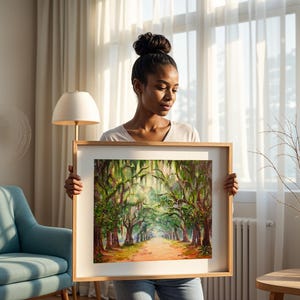 May include: A framed landscape painting showing a tree-lined path with sunlight filtering through the branches. The artwork uses a warm colour palette with greens, browns, and oranges. The frame is made of light-coloured wood.