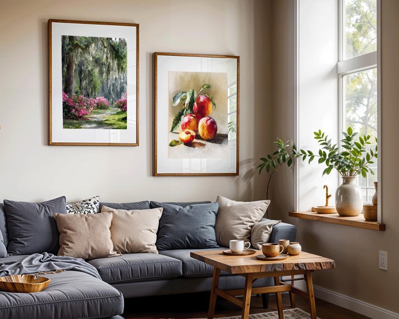 May include: Two framed art prints hang above a gray sectional sofa. One print depicts a path through a lush green and pink floral landscape. The other shows a still life of ripe peaches. A wooden coffee table and decorative items complete the scene.