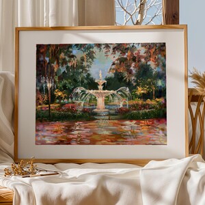 Op de afbeelding: Een ingelijst schilderij toont een fontein in een weelderige tuin. Het kunstwerk toont een centrale fontein met stromend water, omringd door bomen en kleurrijk gebladerte. Het schilderij is gevat in een houten lijst, met een witte passe-partout.