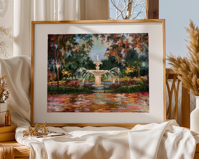 Op de afbeelding: Een ingelijst schilderij toont een fontein in een weelderige tuin. Het kunstwerk toont een centrale fontein met stromend water, omringd door bomen en kleurrijk gebladerte. Het schilderij is gevat in een houten lijst, met een witte passe-partout.