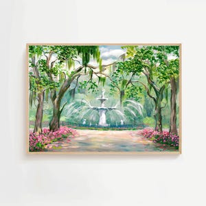 Op de afbeelding: Een ingelijst schilderij van een parkscène met een fontein. Groene bomen omringen de fontein en roze bloemen omzomen het pad. Het kunstwerk heeft een lichte houten lijst en een zachte, schilderachtige stijl.