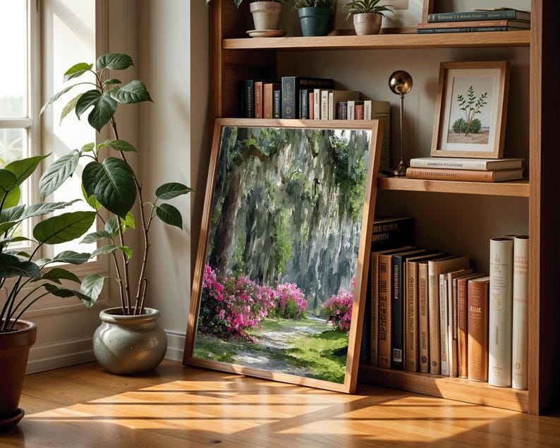May include: A framed landscape painting of a path through a forest with pink flowers. The painting is leaning against a wooden bookshelf filled with books and small potted plants. The room has hardwood floors and a window.