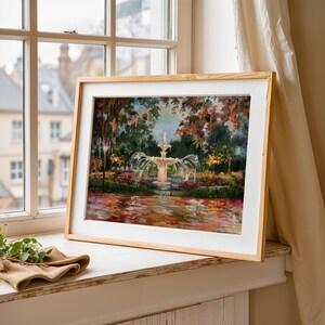 Op de afbeelding: Een ingelijst kunstwerk dat een fontein in een tuin weergeeft. Het schilderij toont een gedetailleerde fontein met water dat in een vijver stroomt, omgeven door weelderig groen en kleurrijke bloemen. De lijst is van lichtgekleurd hout.