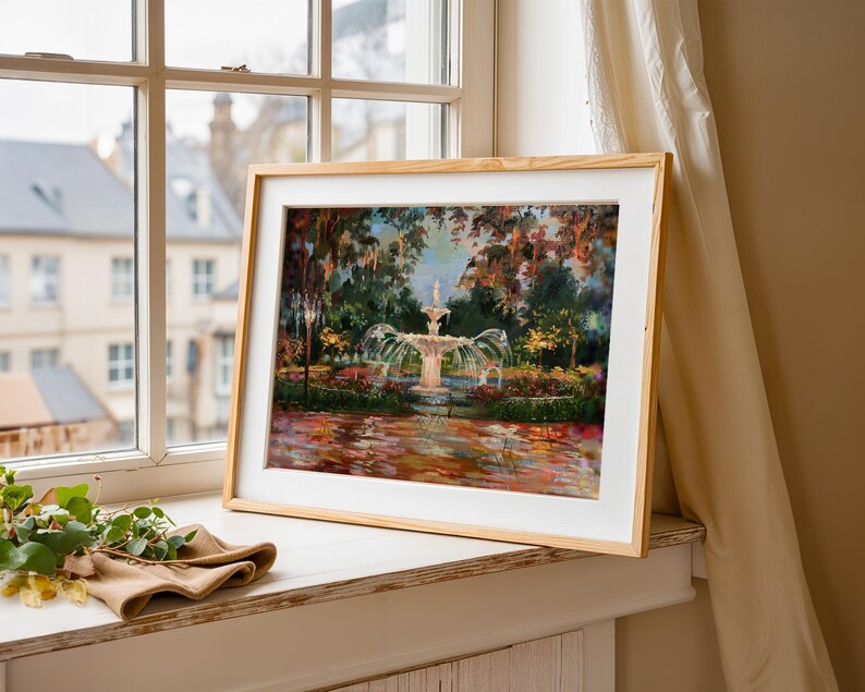 Op de afbeelding: Een ingelijst kunstwerk dat een fontein in een tuin weergeeft. Het schilderij toont een gedetailleerde fontein met water dat in een vijver stroomt, omgeven door weelderig groen en kleurrijke bloemen. De lijst is van lichtgekleurd hout.