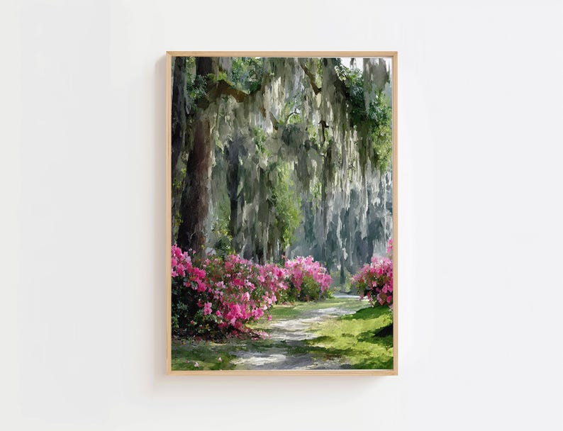 May include: A framed landscape print depicts a path winding through a lush forest. Pink flowering bushes line the path, with Spanish moss hanging from the trees. The artwork is in a wooden frame.