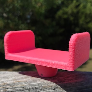 Könnte beinhalten: Ein rosa Plastik-Telefonständer mit abgerundeter Basis. Der Ständer ist so konzipiert, dass er ein Telefon aufrecht hält.