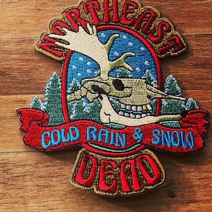以下が含まれることがあります： 「Northeast Cold Rain & Snow Dead」というテキストと、赤い、白い、青い刺繍が施された、ヘラジカの頭蓋骨の入ったパッチです。