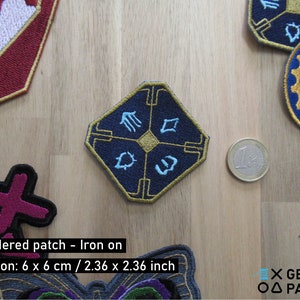 Pode incluir: Um remendo bordado de ferro azul e dourado com um design geométrico. O remendo mede 6 cm por 6 cm.