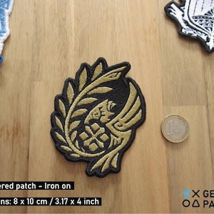 Könnte beinhalten: Gold gestickter Bügel-Patch mit einem stilisierten Design eines Vogels mit ausgebreiteten Flügeln und einem Blattzweig. Der Patch ist 8 x 10 cm oder 3,17 x 4 Zoll groß.