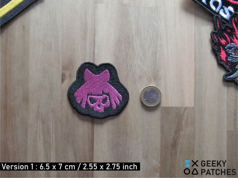 May include: Black embroidered patch with a pink skull and hair design. The patch is 2.55 inches by 2.75 inches.