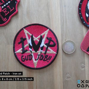 Pode incluir: Patch vermelho bordado para passar a ferro com um pentagrama branco e o texto "IMP GUD JOB!" em letras brancas.