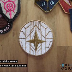 Peut inclure: Patch brodé thermocollant avec un motif géométrique blanc et or avec une étoile au centre. Le patch mesure 9 cm sur 9 cm.