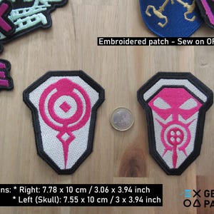 Puede incluir: Dos parches bordados para planchar. El parche de la izquierda es blanco con un símbolo rosa. El parche de la derecha es blanco con un símbolo de calavera rosa. El texto de la imagen dice "Parche bordado - Coser o planchar" y "Dimensiones: * Derecha: 7,78 x 10 cm / 3,06 x 3,94 pulgadas * Izquierda (Calavera): 7,55 x 10 cm / 3 x 3,94 pulgadas".