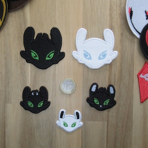 May include: Six embroidered patches featuring the faces of dragons from the How to Train Your Dragon franchise. The patches are black, white, and red. The dragons have green eyes.
