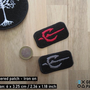 May include: Two embroidered iron-on patches featuring a stylised trident design. The top patch has a red trident on a black background. The bottom patch has a grey trident on a black background. The patches are 6 cm by 3.25 cm, or 2.36 inches by 1.18 inches.