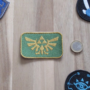 May include: A green and gold embroidered patch featuring the Triforce symbol from the Legend of Zelda video game series.