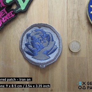 Peut inclure: Un patch brodé gris thermocollant avec un motif de fleur bleue. Le patch mesure 9 cm x 8,5 cm.