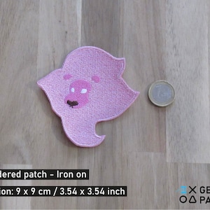 Puede incluir: Parche de hierro bordado de color rosa con la cabeza de un león rosa con la nariz negra y los ojos blancos. El parche mide 9 cm por 9 cm.