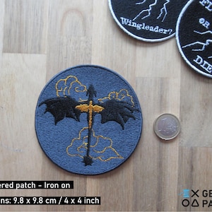Pode incluir: Patch bordado para passar a ferro com um dragão preto com detalhes dourados a voar através das nuvens. O patch mede 9,8 cm por 9,8 cm e tem o texto "Wingleader?" e "Fly or Die" em outros patches no fundo.