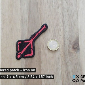 May include: Red embroidered iron-on patch with a black and red design. The patch is 9 cm by 4.5 cm.