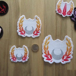 May include: Three embroidered patches with a white background and a crescent moon design. The patches have a red and orange wreath around the moon.