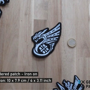 May include: White and black embroidered iron-on patch featuring a dragon design. The patch is 4 inches by 3.11 inches.  Embroidered patch - Iron on. Dimension: 10 x 7.9 cm / 4 x 3.11 inch. X GEEKY PATCHES