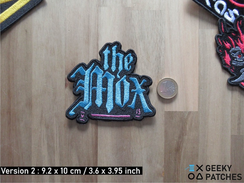 May include: A blue and black embroidered patch with the text "the Mox" in a gothic font. The patch is 3.6 inches by 3.95 inches.