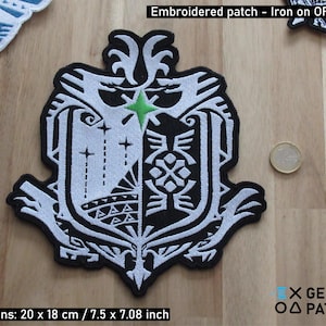 May include: Black and white embroidered patch with a green star in the center. The patch features a shield design with intricate details and the text "X GEEKY ΟΔ PATCHES". The patch is 7.5 inches by 7.08 inches.