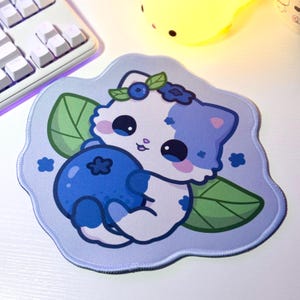 May include: A blue and white cartoon cat with a blueberry in its paws. The cat is wearing a flower crown and is surrounded by green leaves. The background is a light blue color.