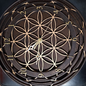 May include: A dark brown wooden clock with a flower of life design and gold-coloured numbers. The clock face is surrounded by multiple concentric rings.