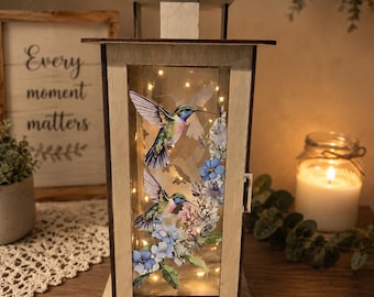 Farol de madera artesanal con diseño de colibrí y flores silvestres, con luz LED cálida.