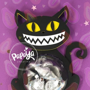 Puede incluir: Porta golosinas con forma de gato negro con una cara sonriente y un recipiente de plástico transparente para guardar golosinas. El porta golosinas está hecho de madera y tiene un diseño recortado. El fondo es un patrón morado y rosa con fruta de papaya.