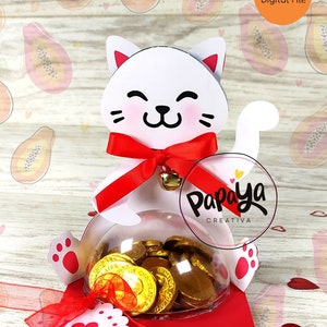 Puede incluir: Una caja blanca con forma de gato con un lazo rojo y una cúpula de plástico transparente llena de monedas de oro. La caja está sentada sobre una tarjeta roja y blanca con la palabra "LOVE" en ella. El fondo es un patrón rosa y naranja de fruta de papaya.