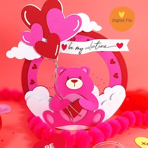 May include: A pink teddy bear holding a heart sits in a pink and red heart-shaped frame with a cloud and balloons. The text "be my valentine" is written on a banner above the bear. The background is pink with a pattern of papaya fruit.