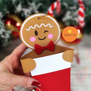 Puede incluir: Un modelo imprimible de porta calcetines de jengibre. El hombre de jengibre es marrón con glaseado blanco y una pajarita roja. El calcetín es rojo con un puño blanco. La imagen incluye el texto "Archivo digital" y "Papaya Creativa".