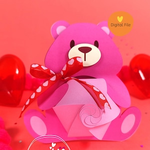 Puede incluir: Oso de papel rosa sosteniendo una caja de corazón rosa y blanca con una cinta roja y lunares blancos. El oso tiene una nariz roja y ojos negros. El fondo es rosa con corazones blancos y el texto "Papaya Creativa" en un círculo rosa.