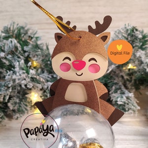 Puede incluir: Un archivo digital para un adorno navideño con un reno sosteniendo una esfera de plástico transparente. El reno es marrón con la nariz roja y las mejillas rosadas. La esfera está llena de monedas de chocolate doradas y plateadas. El texto "Digital File" está en una etiqueta rosa en forma de corazón.