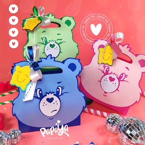 Puede incluir: Tres cajas de regalo con forma de oso de colores verde, azul y rosa, cada una con un asa y una cara sonriente. Las cajas tienen lazos y adornos decorativos. Las cajas están sobre una superficie rosa con bolas de discoteca y bastones de caramelo.