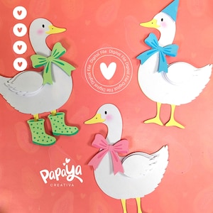 May include: Three white paper cut-out geese with yellow beaks and feet, each adorned with a different accessory: a green bow and boots, a blue party hat and bow, and a pink bow. The background is a coral color with a heart pattern and the text "Papaya Creativa".