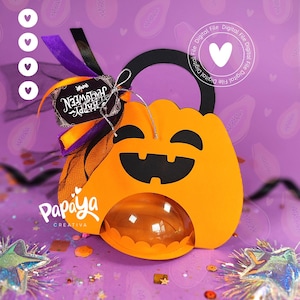 May include: Orange pumpkin-shaped Halloween treat container with a black handle and face. The container has a clear, rounded front and is decorated with purple and orange ribbons, a tag that says "Happy Halloween", and the "Papaya Creativa" logo.