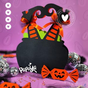 May include: A black cauldron-shaped paper craft with orange and green accents, topped with witch's hat details and orange ribbons. The design includes a smiling candy cutout and the text "Papaya Creativa". Decorative disco balls are scattered around.